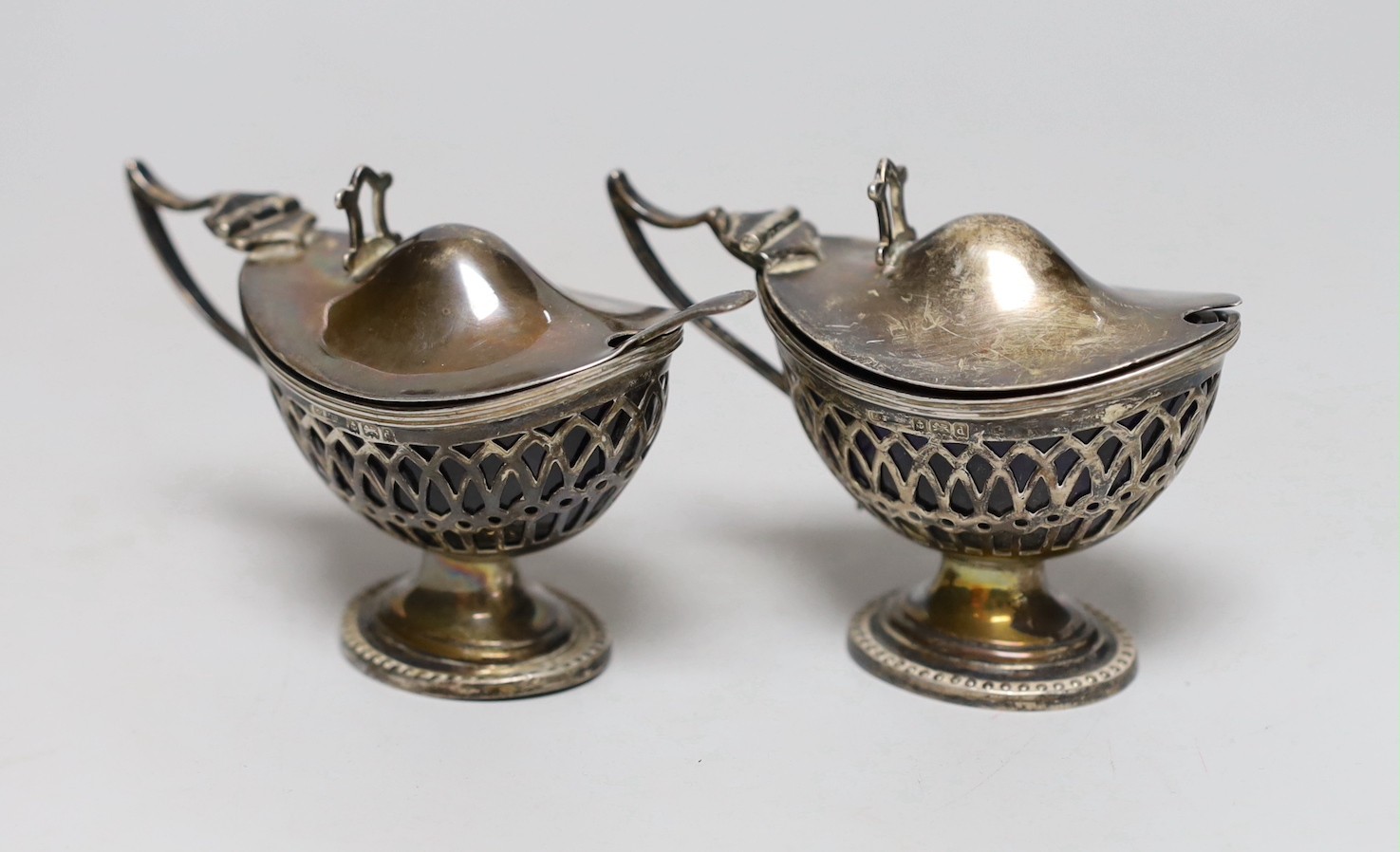 A pair of Edwardian pieced silver pedestal boat shaped mustard pots, E.S. Barnsley & Co, Birmingham, 1903, length 91mm, one with associated silver condiment spoon.